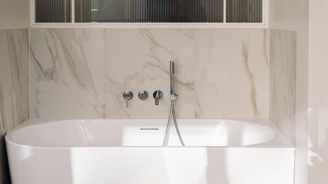 Freestanding white bathtub with marble tile walls in modern bathroom