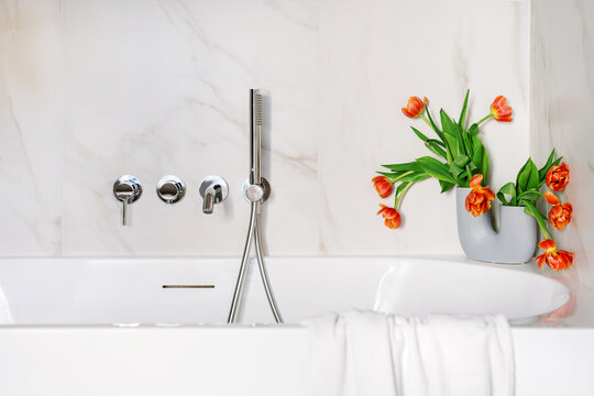 White bathtub with chrome shower and orange tulips on marble