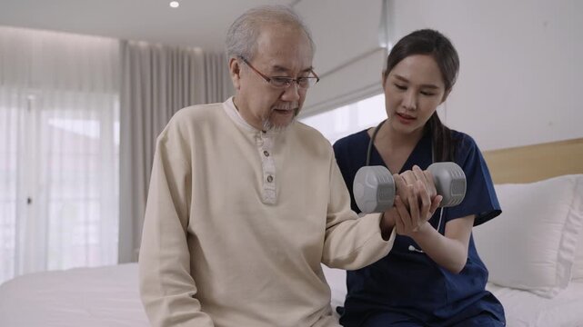 Professional Asian woman nurse physiotherapist using a dumbbell for workout exercise for physical recovery of muscles and bones of a senior man patient in hospital bed. Healthcare and medical concept.