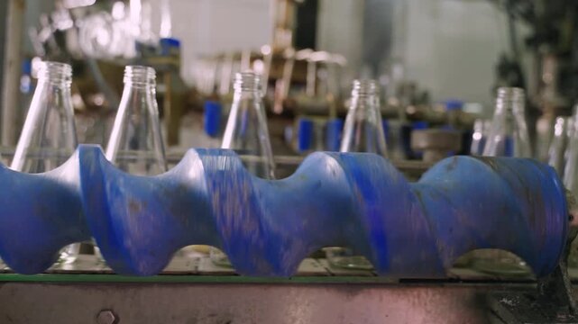 Empty glass beverage bottles on an automatic conveyor belt in a manufacturing plant. Technology for manufacturing bottles and filling fruit juice. Drinking water bottle on factory production conveyor.