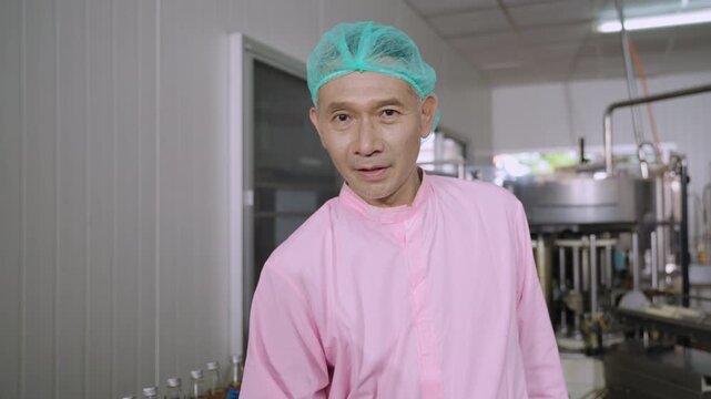 Professional Asian inspector in uniform of food and drink factory holding a juice beverage bottle promoting and advertising healthy nutritional benefits in production line at a manufacturing industry.