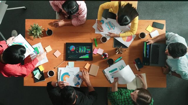 Top view of skilled businessman present marketing idea at meeting while group of investor listening and planning strategy while looking at stock market chart or data analysis document. Convocation.