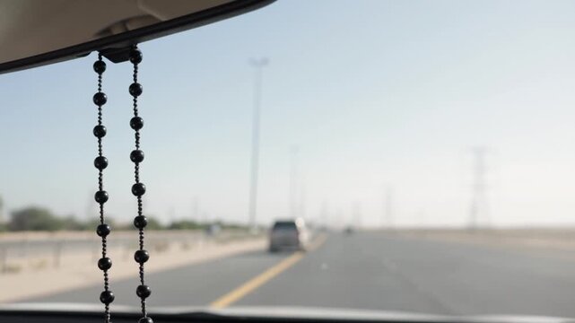 Misbaha, or prayer beads, hanging from a rearview mirror while driving through a desert highway