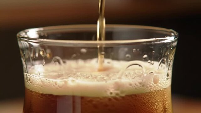 Close-up of dark beverage pouring into a textured glass, creating foam.