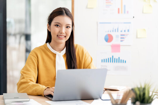Confident Young Asian Businesswoman Smiling at Camera While Typing on Laptop