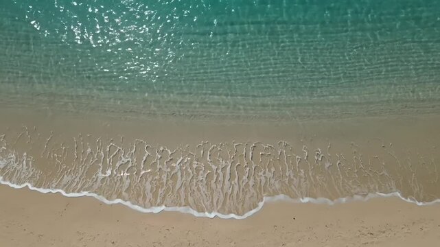 Aerial view of ocean waves on sandy beach shore.