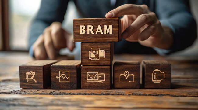 Hands stacking wooden blocks labeled BRAM with business icons on a rustic table, conveying focused planning, organization and professional strategy