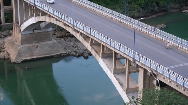An arched concrete bridge carries cars and scooters over a green river in Yizhou, Guangxi, China. Chinese road infrastructure, river crossings, and transportation in regional city. 广西宜州 