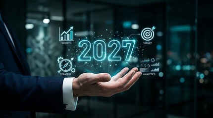 Fototapeta premium Businessman's hand holding glowing year 2027 with business growth icons during night office setting