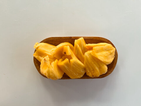 Bright yellow jackfruit pieces served in a wooden bowl on a white surface