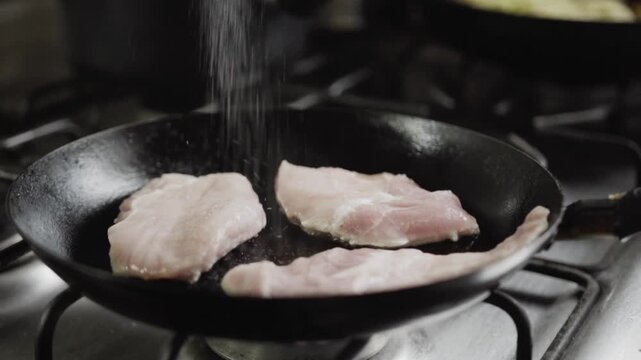 Close up of pork loin cooking in frying pan on gas stove with rising steam highlighting meat preparation, sizzling texture and culinary process in commercial kitchen