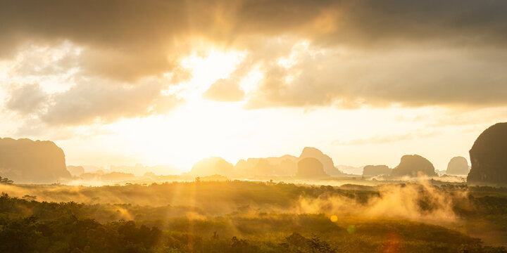 Majestic sunrise landscape background with golden sun rays piercing through morning mist over limestone karst mountains for panoramic travel design