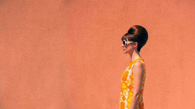 Side profile of a retro 1960s woman with a beehive hairstyle and sunglasses against a solid orange wall