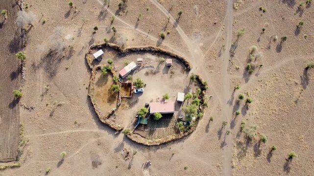 Drone footage of a modern Maasai boma in rural Kenya featuring contemporary homes, a traditional livestock enclosure, cattle boma, cultivated garden, and a fenced homestead in the African savannah.