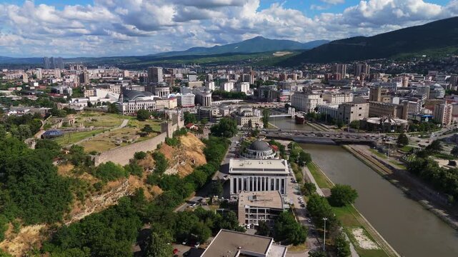 Drone wide aerial view of Skopje cityscape flanking the Vardar river riverbed. Metropolitan development and urban residential districts in North Macedonia capital.