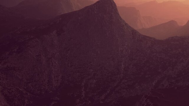 The scene shows a large mountain with a peak surrounded by smaller hills and valleys. The sky has a warm color as the sun sets. This sight brings attention to natures shapes and colors.