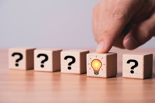 Hand selecting a light bulb icon among question mark blocks represents creative thinking, problem solving, innovation, decision making, business strategy, new ideas and smart solutions for growth.