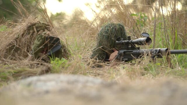 Sniper team hidden in tall grass during military reconnaissance exercise, maintaining covert observation and tactical positioning