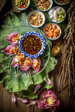 Delicious Miang Kham Bua Luan, a traditional Royal Thai appetizer featuring vibrant pink lotus petals, toasted coconut, fresh herbs, and sweet savory dipping sauce served on a wooden table.