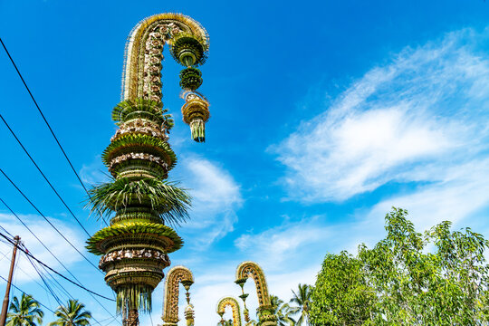 Tall, elaborate Balinese penjor decorated with woven coconut leaves standing against a bright blue sky during Galungan festival celebrations.