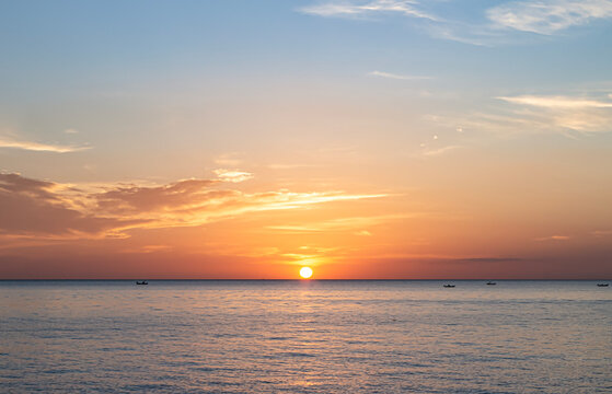 Beautiful sunset sea landscape background with small sun disk on horizon and soft pastel orange clouds for panoramic beach travel design