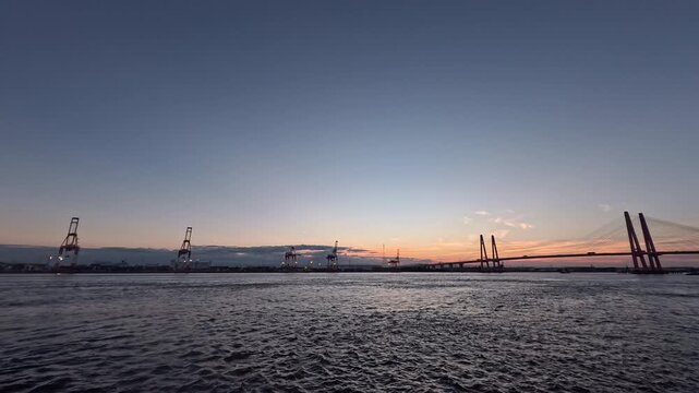 Real-time maritime industrial footage of the Port of Nagoya shipping infrastructure under a dim sunset sky