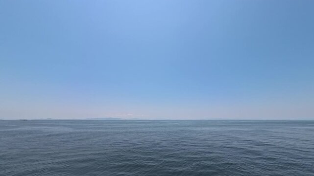 Cinematic video of a vast deep blue ocean under a clear sunny sky with faint distant islands