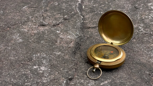 An open brass compass rests on a textured stone. The minimalist composition highlights the texture of the natural material and is suitable for concepts of navigation, route selection, tourism, design,