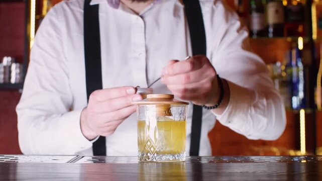 Modern cocktail preparing. Alcohol beverage. Unrecognizable skillful bartender male hands making drink in glass using tool flaming liquid decoration on bar counter.