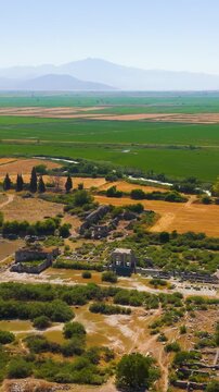 Vertical video. Balat, Turkey. Aerial view over the ancient ruins of Miletus, revealing the Delphinion sanctuary, Capito Roman Baths and North Agora amid sun-baked fields and distant mountains. Aeria