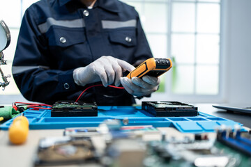 Technician in gloves tests computer hard drives with a handheld meter at an electronics repair bench, showing data recovery, maintenance, and hardware diagnostics in a clean workspace © Thitaporn