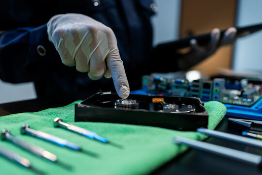 Close-up of a technician in gloves pointing at an opened hard drive on a workbench with repair tools, showing computer data recovery, maintenance, and hardware inspection.
