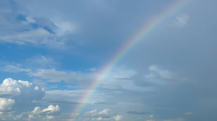 Fototapeta premium Brilliant pastel rainbow arching across vast blue sky with soft white clouds