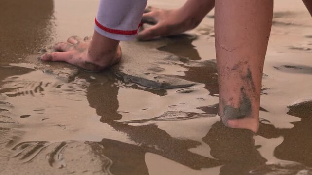 A young child playing on wet beach sand and burying their feet while enjoying a day at the seaside