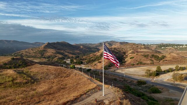 A beautiful aerial sweep around a gracefully waving American Flag. As the drone gently glides from one side to the other the scene opens up to mountains and blue skys surrounding Old Glory
