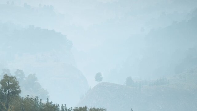 Fog covers a wide landscape with mountains and hills. Trees are barely visible in the mist. This scene shows the calm of nature during a morning in an outdoor area.