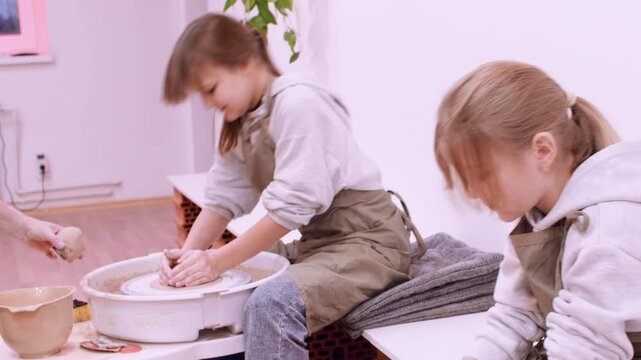 Diy craft. Artisan master class. Professional woman teaching girls handmade ceramic using electric wheel in workplace indoor.