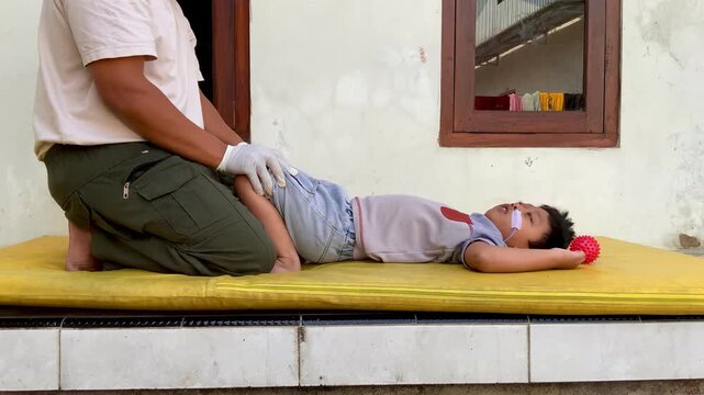 Father helping his young son with pediatric physical therapy leg stretching exercises at home
