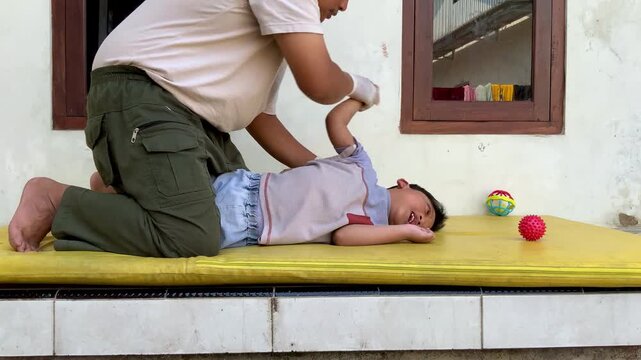 A father performing passive range of motion exercises on a child with cerebral palsy to improve joint mobility and reduce muscle tightness at home