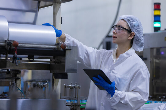 female worker wearing uniform inside factory clean room conducting inspection on manufacturing machine holding digital tablet monitor process carefully