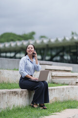 Obraz premium Woman multitasking outdoors, talking on smartphone and using laptop