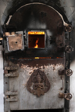 Old crematorium furnace door with burning fire and buddhist angel carving in Thai temple