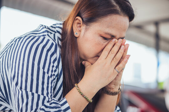 Depressed and stressed Asian middle-aged woman sitting lonely on a bench with head in hands inside an industrial background. Concept of financial crisis, business bankruptcy, debt pressure, mental hea