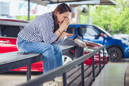 Depressed and stressed Asian middle-aged woman sitting lonely on a bench with head in hands inside an industrial background. Concept of financial crisis, business bankruptcy, debt pressure, mental hea