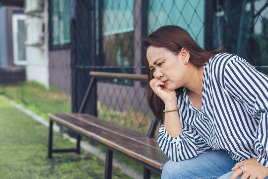 Sad and depressed Asian woman sitting lonely on a bench with anxious expression facing emotional stress. Concept of severe mental health crisis, chronic stress, depression, midlife crisis, personal pr