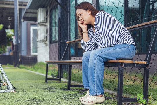Sad and depressed Asian woman sitting lonely on a bench with anxious expression facing emotional stress. Concept of severe mental health crisis, chronic stress, depression, midlife crisis, personal pr