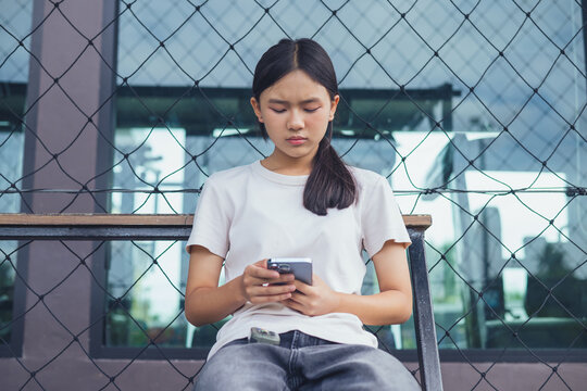 Worried and stressed Asian teenager girl holding smartphone looking at screen with anxious expression. Concept of cyberbullying, social media peer pressure, smartphone digital addiction, and youth men