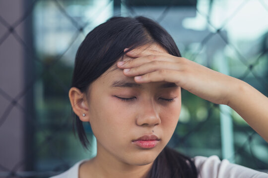 Sad and depressed Asian teenager girl closing her eyes with hand on face facing severe emotional stress. Concept of youth mental health crisis, teenage depression, chronic anxiety, burnout syndrome, p