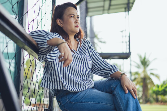 Sad and depressed Asian middle-aged woman sitting lonely on a bench with anxious expression facing emotional stress. Concept of severe mental health crisis, chronic stress, depression, midlife crisis,