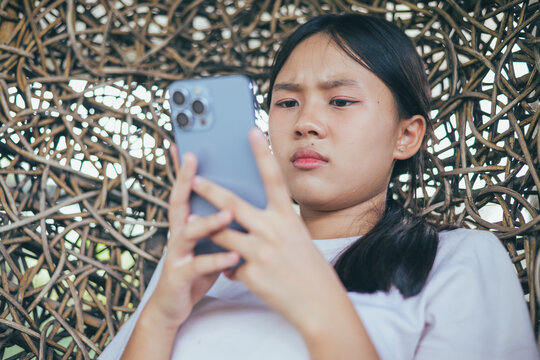 Worried and stressed Asian teenager girl holding smartphone looking at screen with anxious expression. Concept of cyberbullying, social media peer pressure, smartphone digital addiction, and youth men